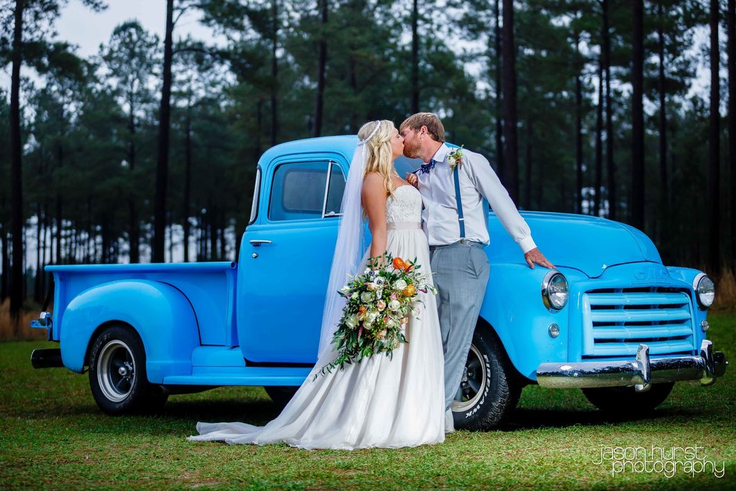 Bride and groom kissing beside a vintage blue truck